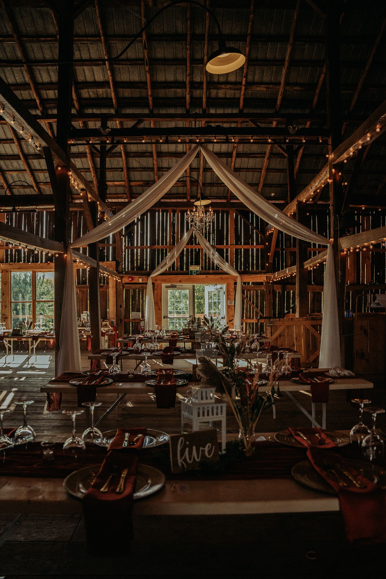 Barn wedding venue interior in Ontario with fairy lights, white chairs, and a spacious reception layout ready for dinner.