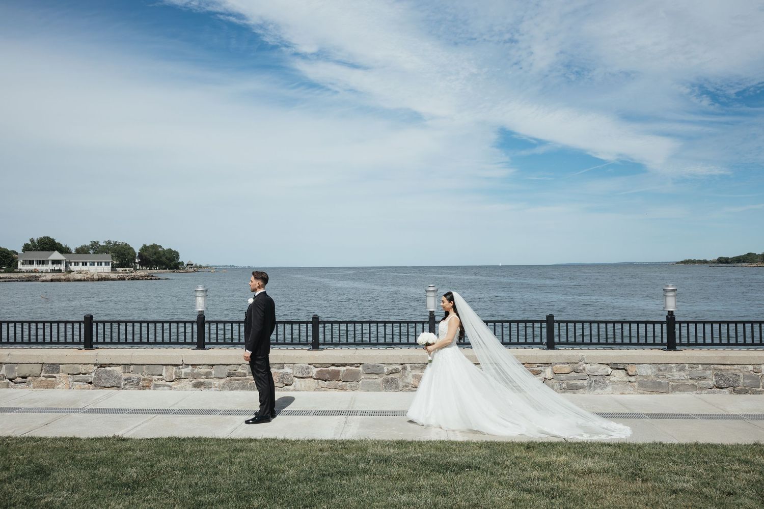 Wedding ceremony setup with white chairs on a lush green lawn facing a historic stone church under cloudy skies.
