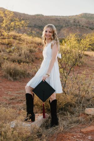 A senior smiles with her graduation cap in Palo Duro Canyon during golden hour.