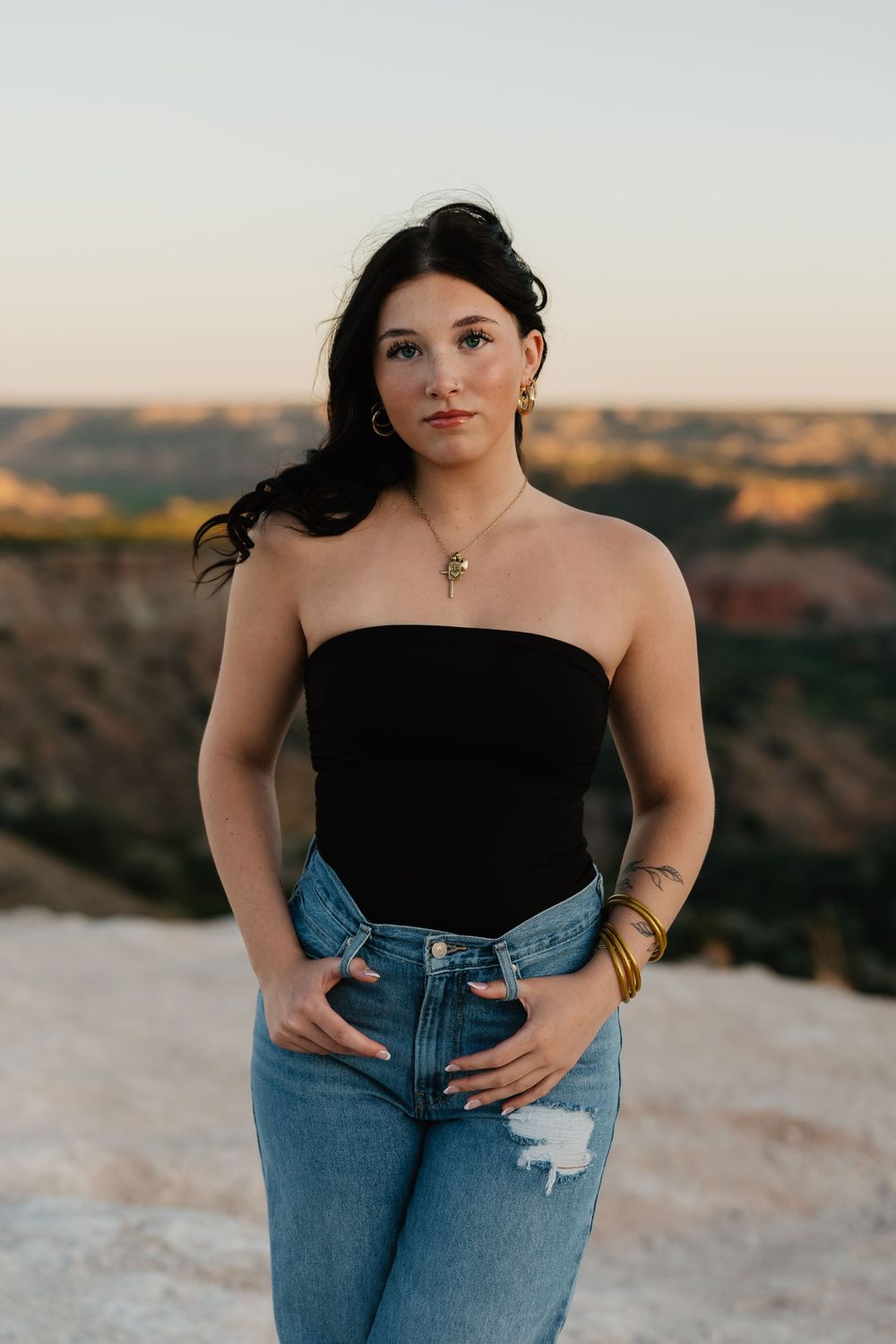 A girl stands at the top of Palo Duro Canyon to pose for senior portraits at sunset.