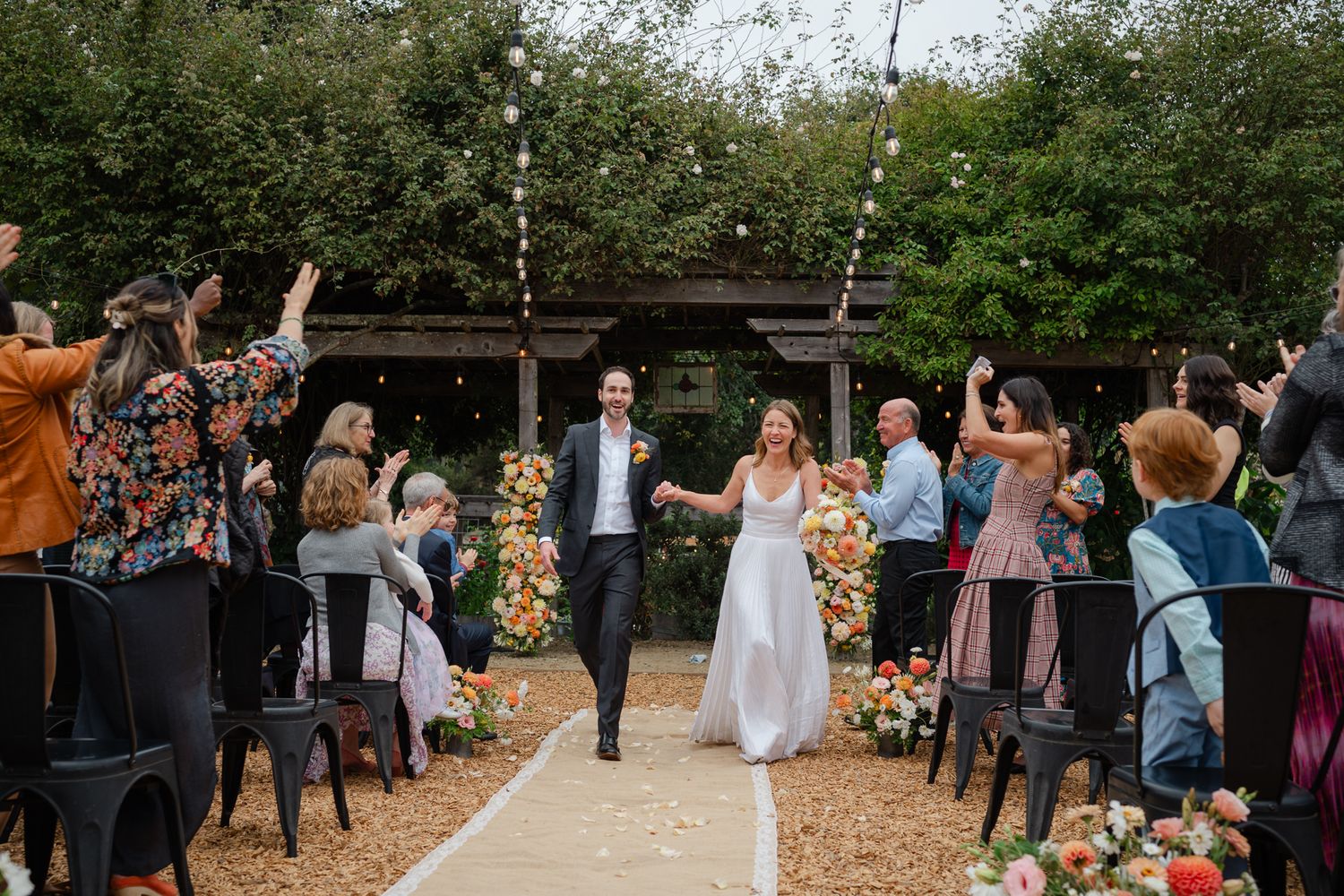 Elegant black and white wedding photo of couple holding hands and dancing joyfully in a grassy meadow.