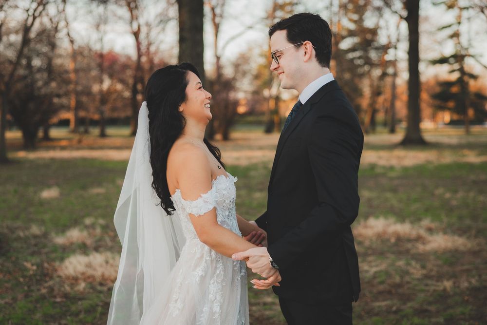 A bride in a lace gown and veil holds hands with a groom in a black suit outdoors at the dc war memorial
