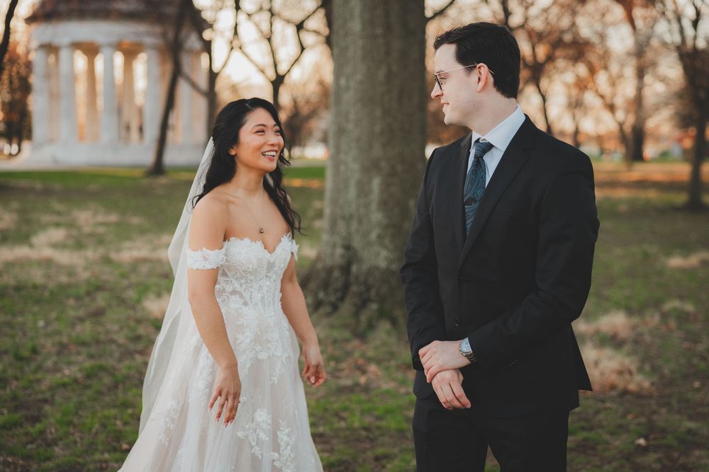 Bride in lace off-shoulder gown and groom in black suit share a joyful first look outdoors near the dc WWII memorial