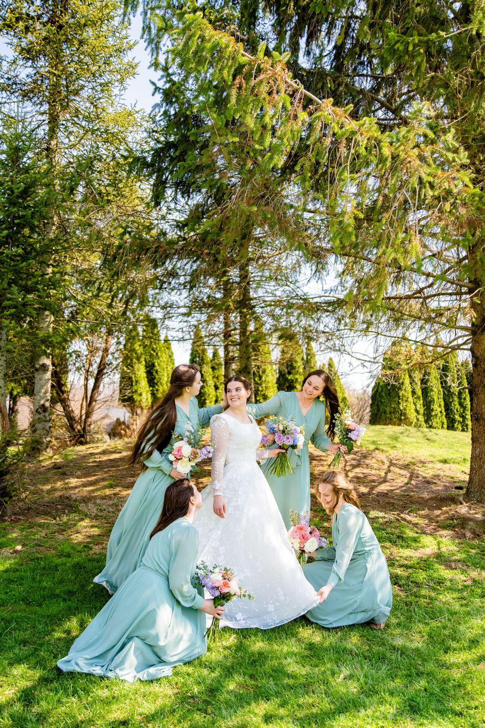 Bride in white gown surrounded by bridesmaids in mint green dresses holding colorful bouquets outdoors.