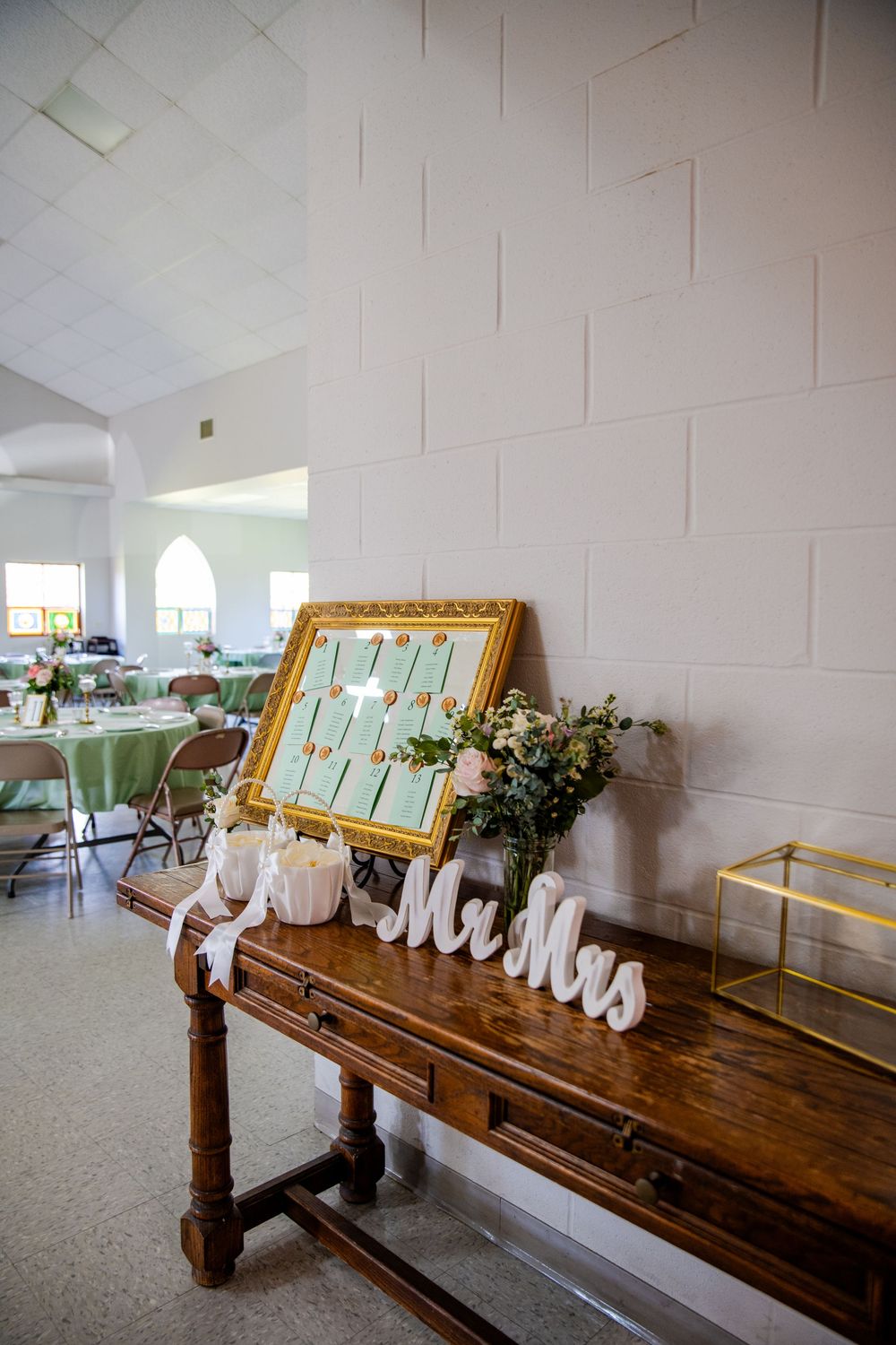 Elegant wedding reception entrance table with Mr and Mrs signs, seating chart in gold frame, and floral arrangement.