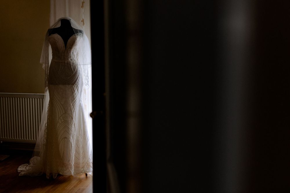 A elegant lace wedding dress displayed on a mannequin, viewed through a doorway in a warmly lit room.