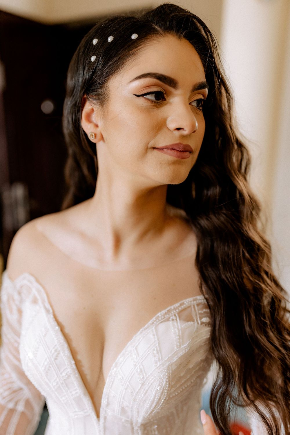 Beautiful bride with pearl hair pins and wavy dark hair in elegant lace wedding dress closeup.