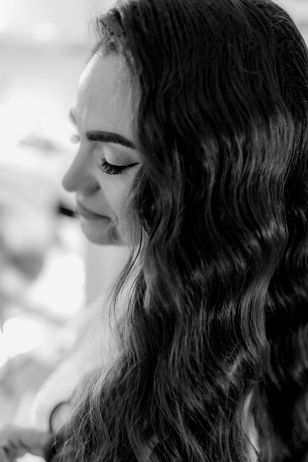 Black and white profile portrait of a young woman with long wavy hair and elegant eye makeup.