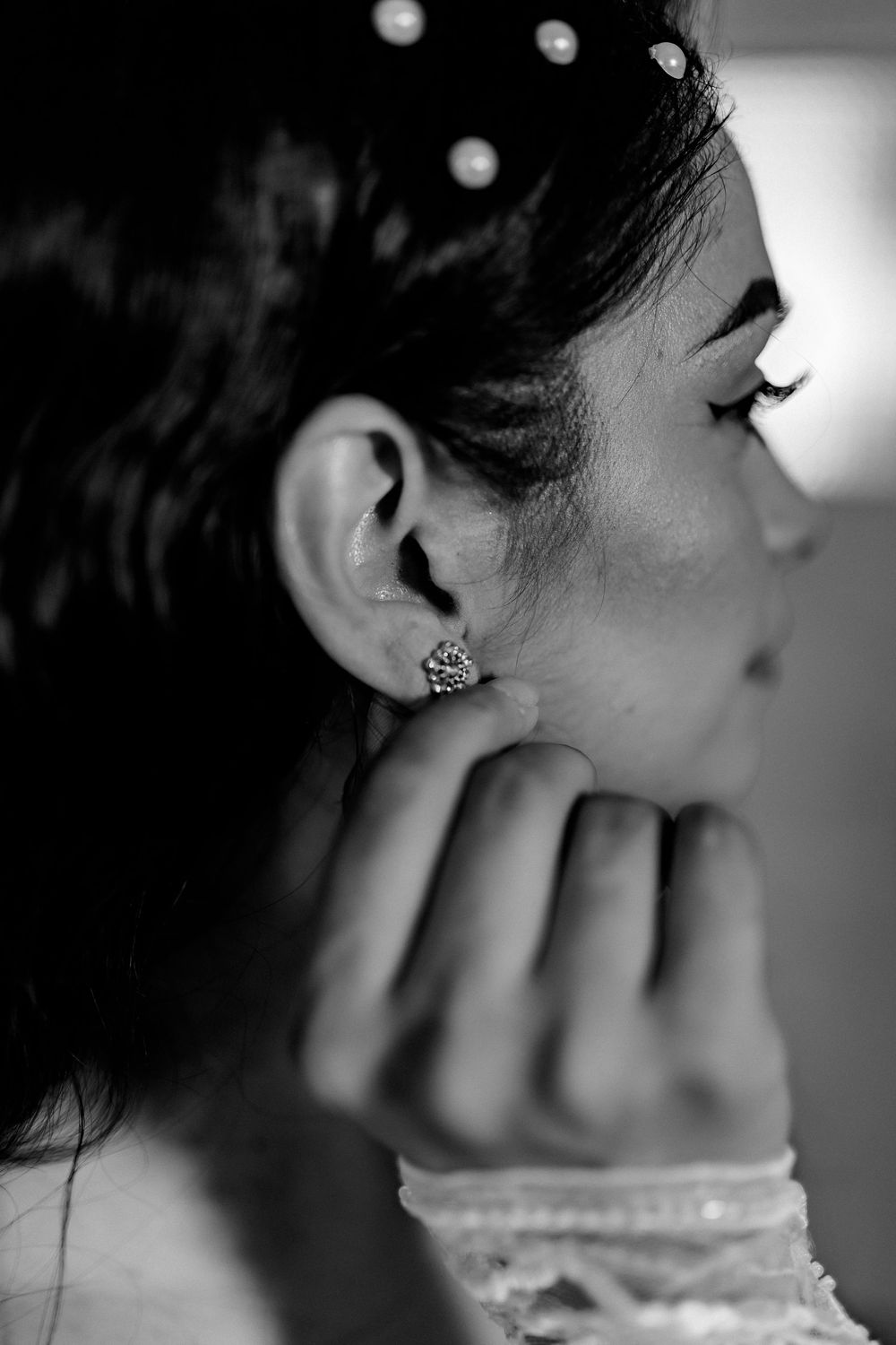 Black and white close-up of a bride adjusting her diamond stud earring with pearl hair accessories.