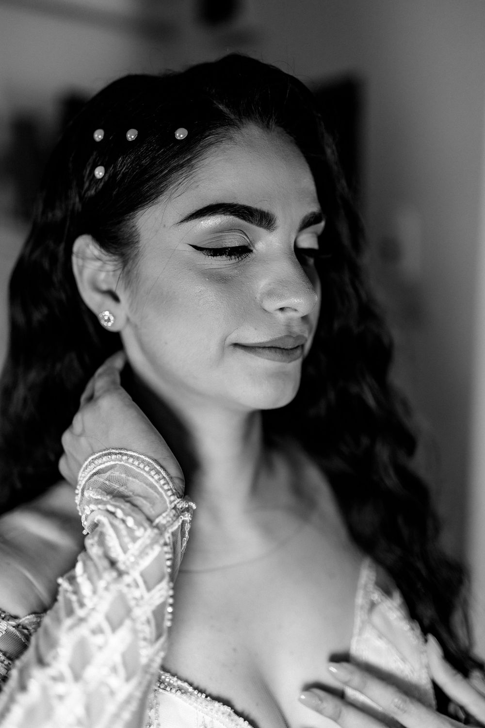 Black and white portrait of a bride with wavy hair, pearl hair pins, and elegant lace wedding dress.