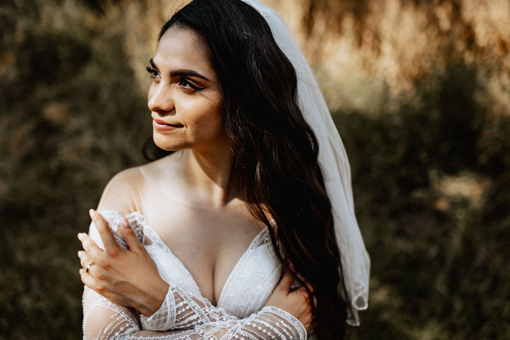Beautiful bride in lace dress with veil gazing away in warm golden sunlight.