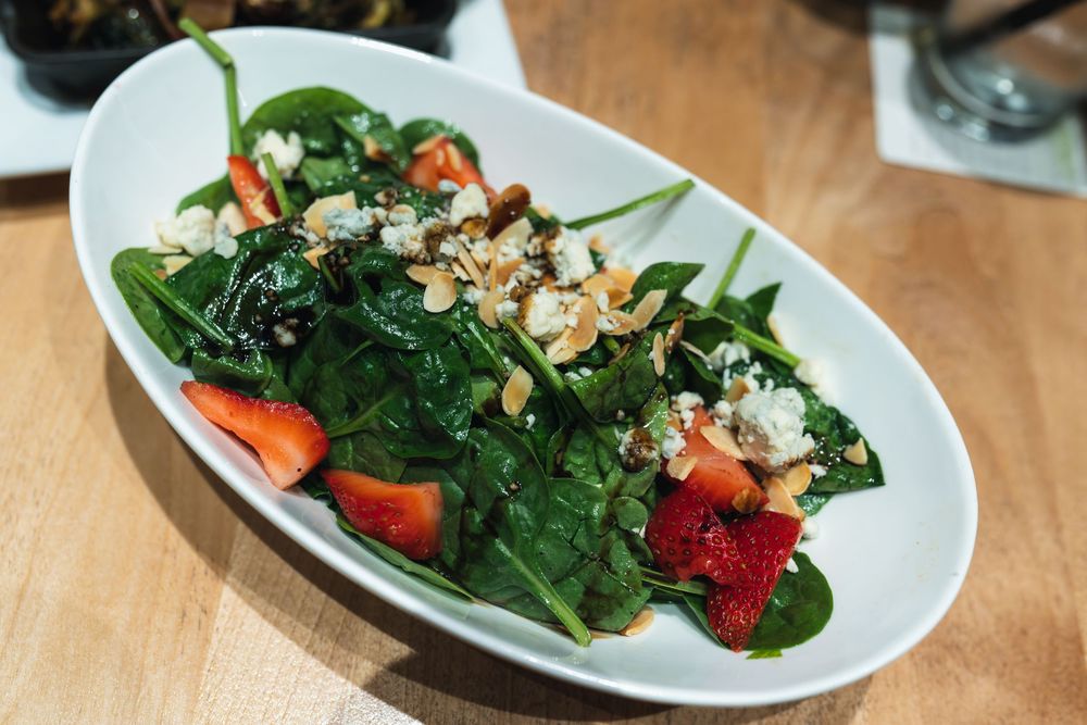 Fresh spinach salad with strawberries, blue cheese crumbles, and toasted almonds served in a white oval dish.