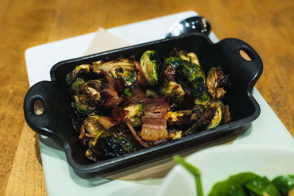Roasted Brussels sprouts with crispy bacon bits served in a black cast iron dish on a white plate.