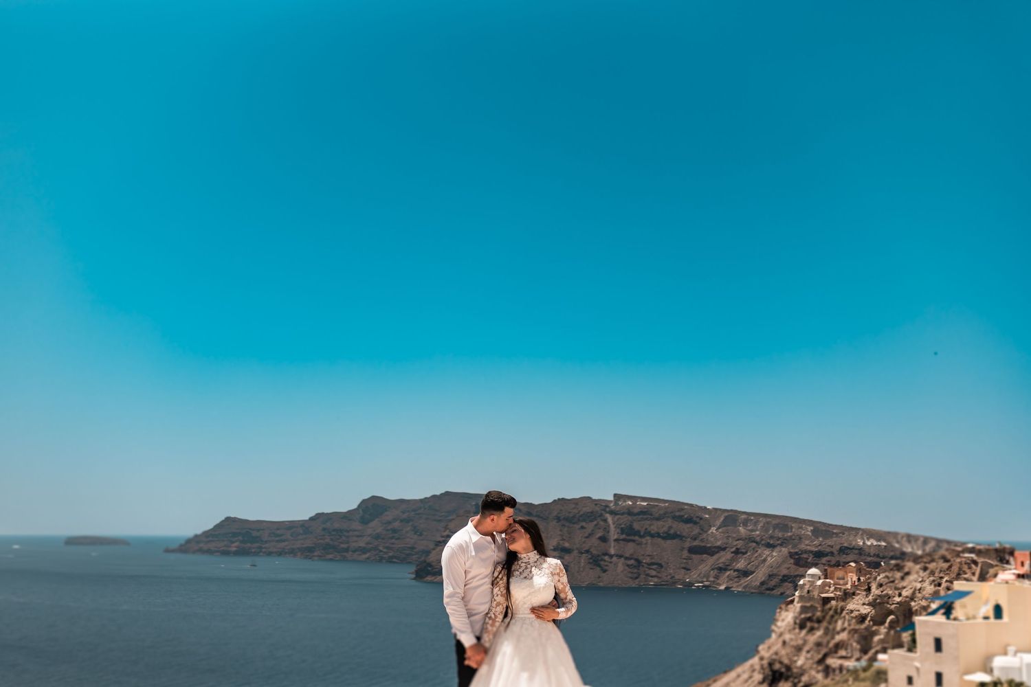 Romantic couple embracing on a cliffside in Santorini, Greece, with stunning blue sea and volcanic caldera views.