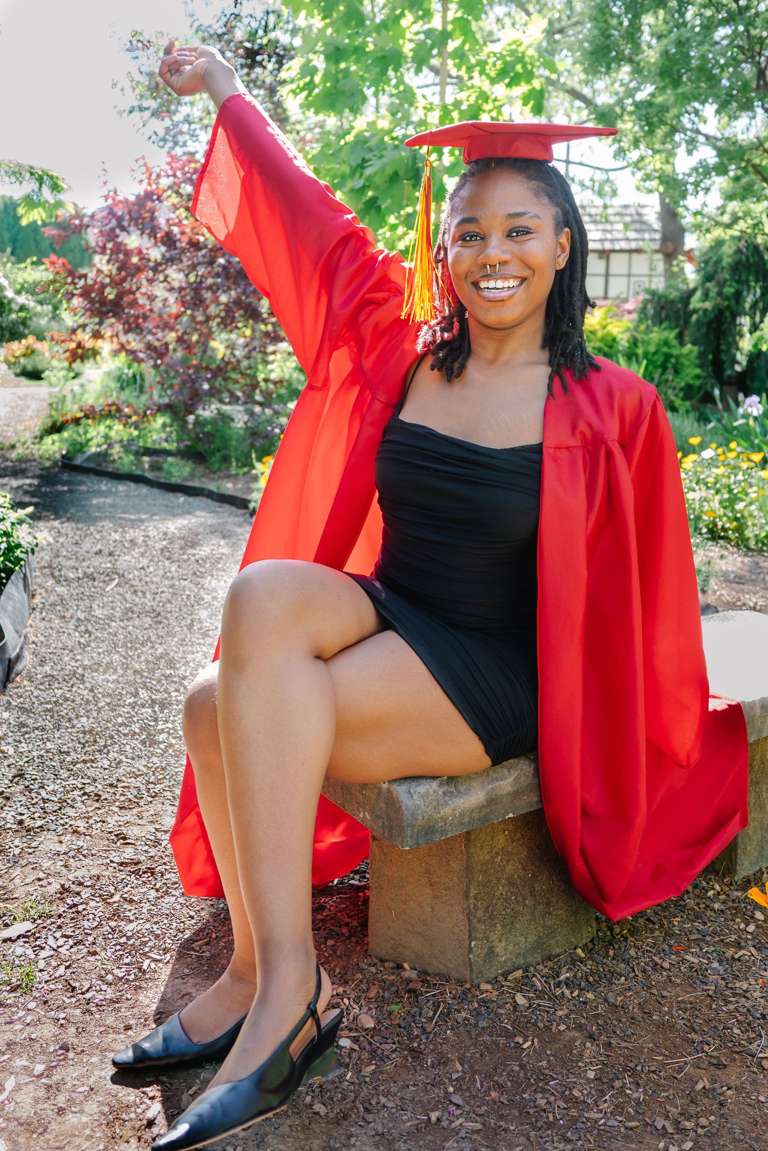 Senior sitting in garden wearing red graduation gown in Washington state