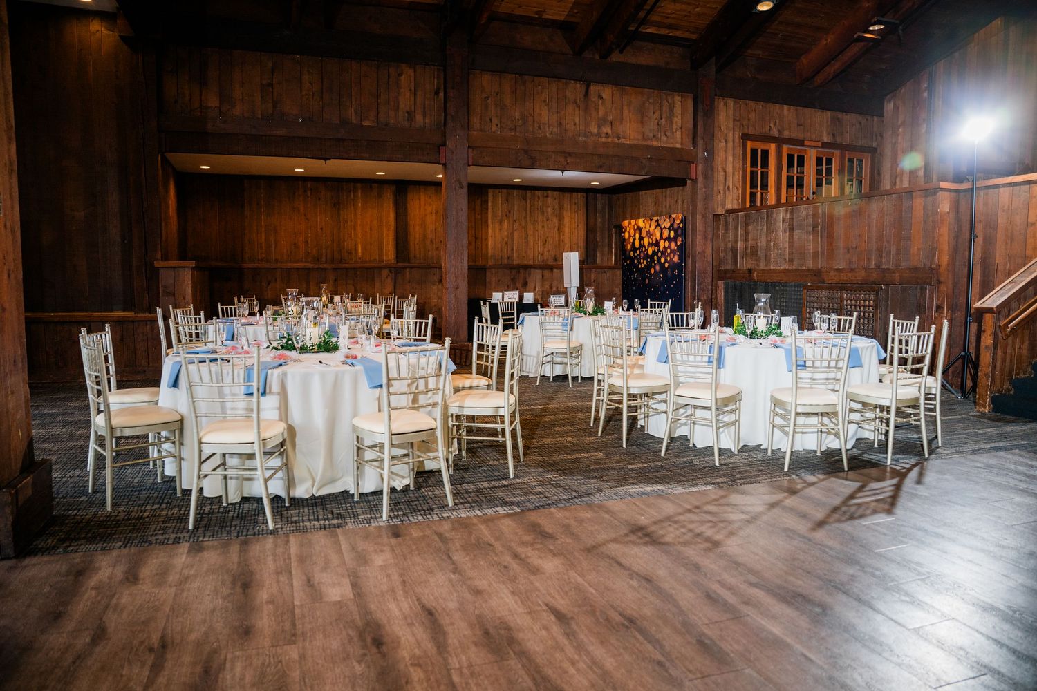 Elegant wedding reception hall with round tables, white chiavari chairs, and wood-paneled walls in a rustic venue.