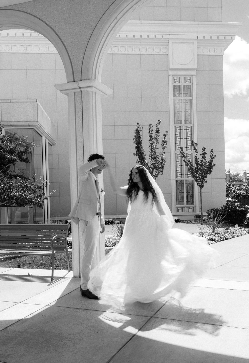 Black and white photo of bride and groom sharing a moment under arched columns at wedding venue.