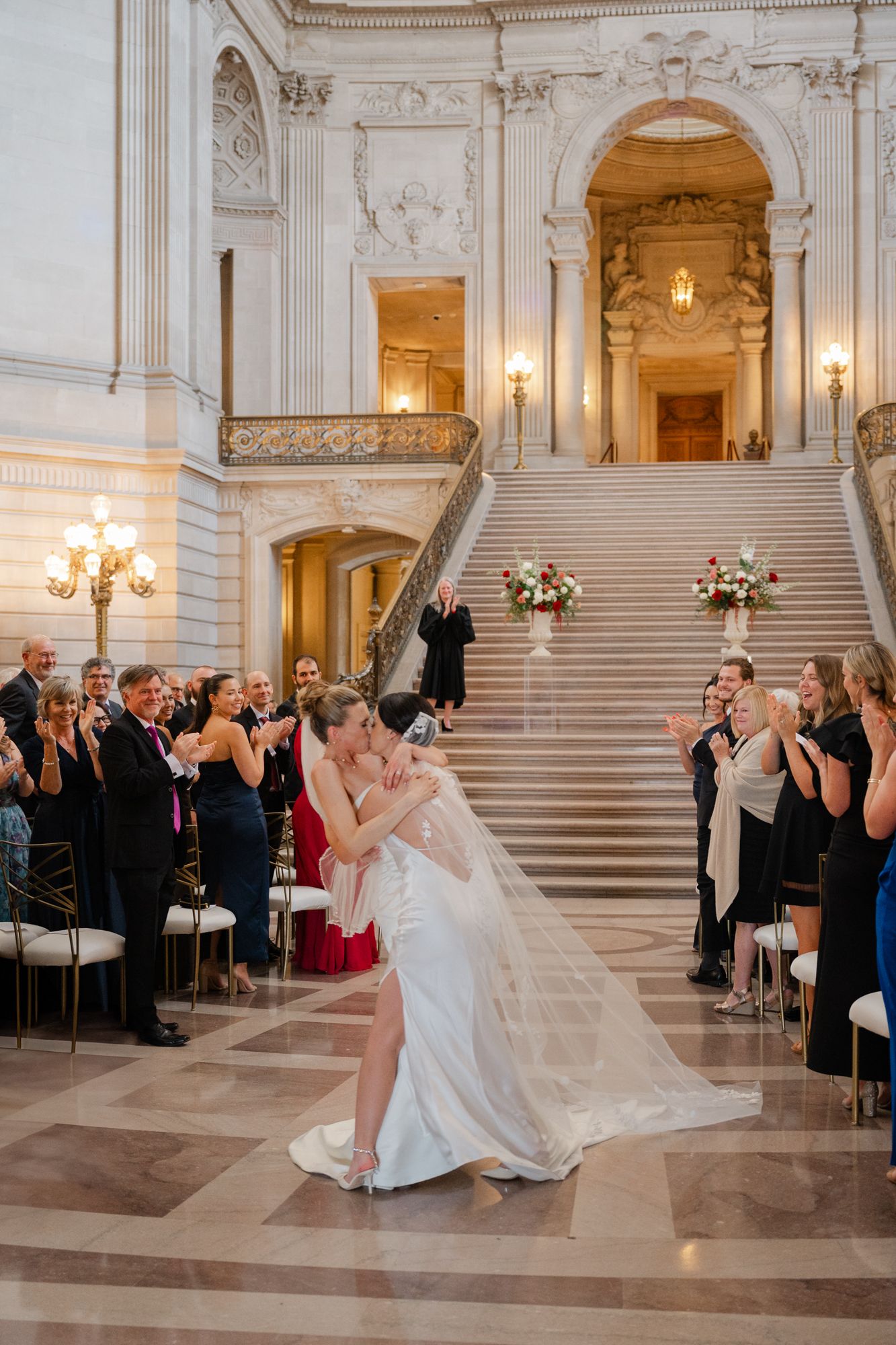Black and white photo of a groom dipping his bride at San Francisco City Hall wedding ceremony with guests applauding.
