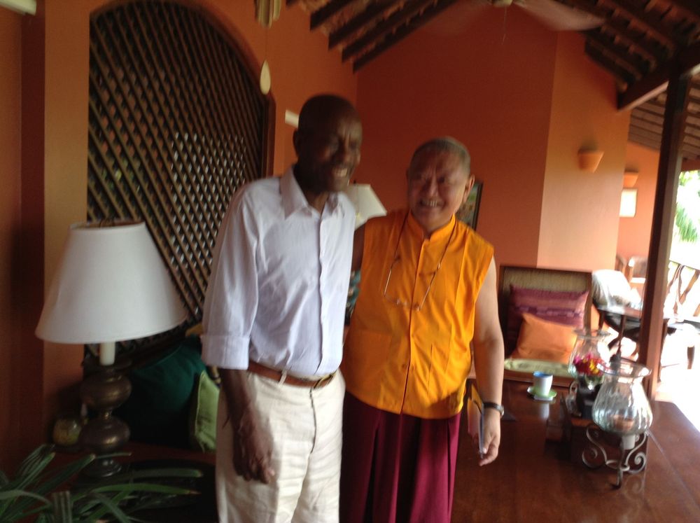 Two people smiling together inside a colorful orange villa with wooden ceiling and tropical decor.