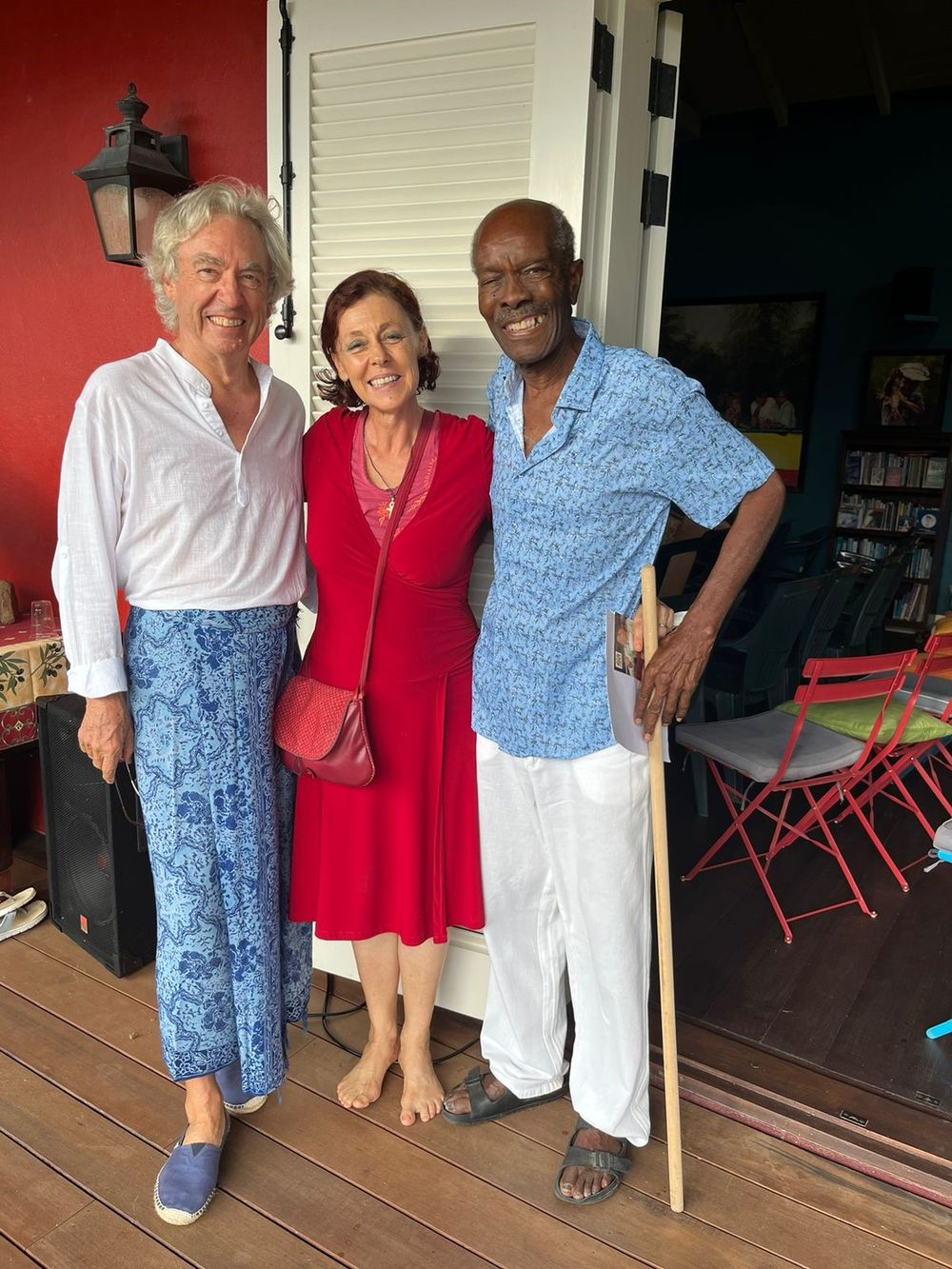 Three friends pose together on a wooden porch, two wearing blue and one in a red dress, smiling warmly.