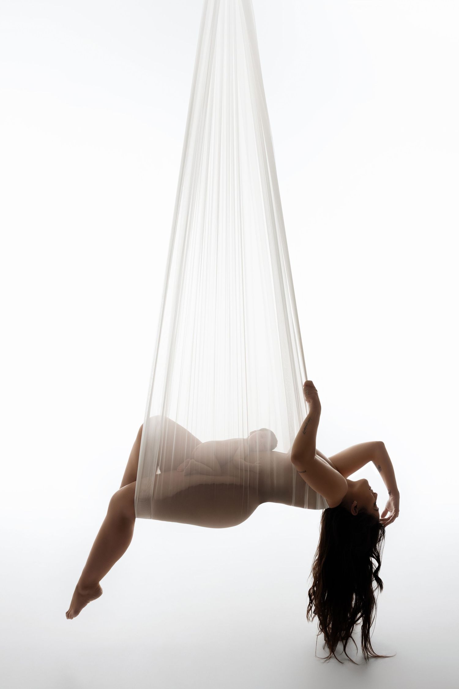 Ethereal maternity photo with suspended white fabric creating floating effect.