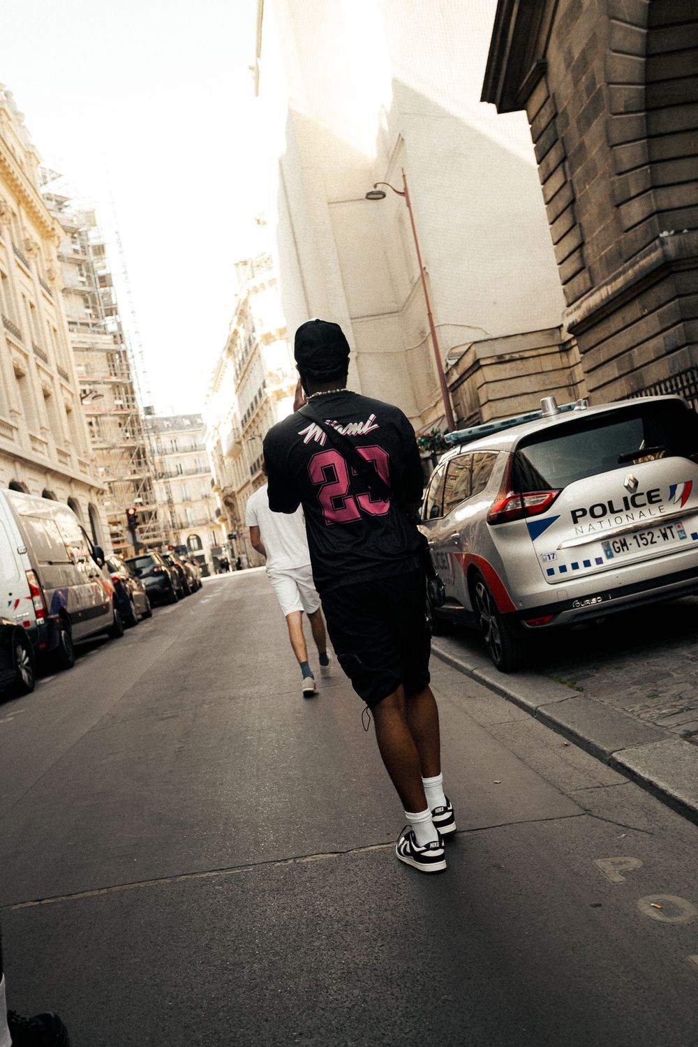 Man in black jersey number 23 walking down a Parisian street past a police car.