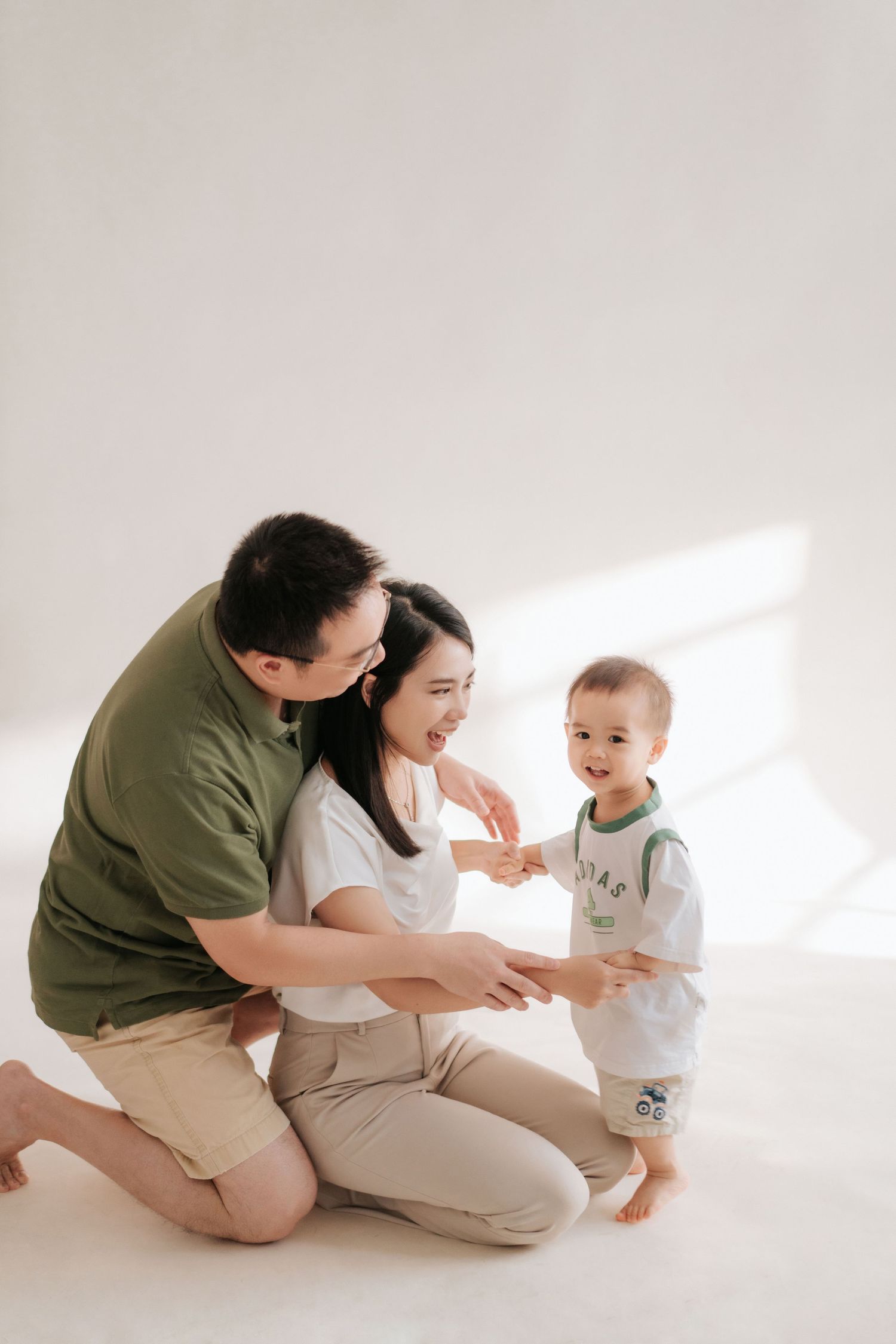 A family in white and olive outfits shares playful moments together in a bright minimalist setting一家人穿著白色和橄欖綠服裝，在明亮簡約的環境中共享歡樂時光。