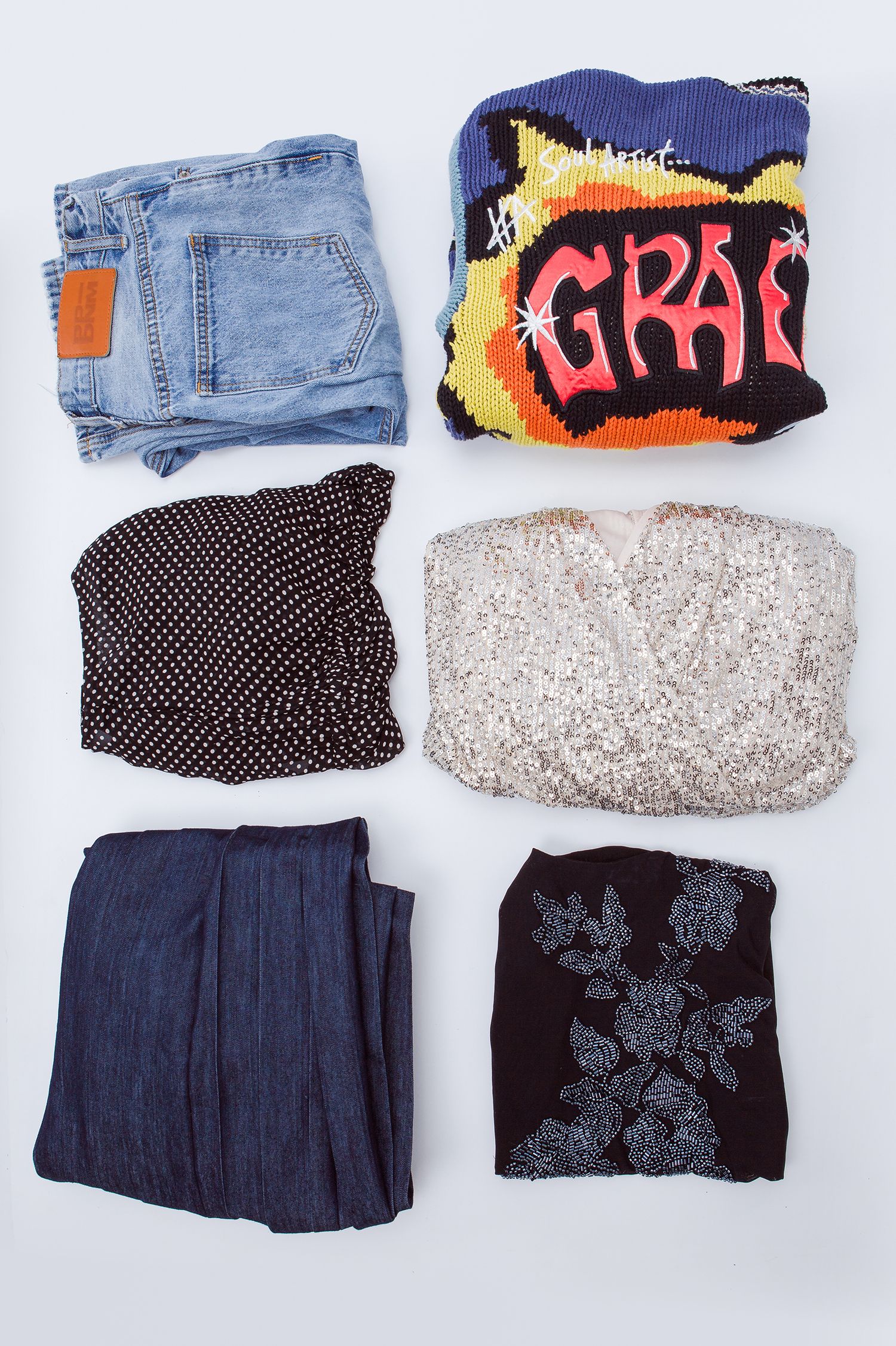 Folded clothing items arranged in pairs showing jeans, colorful socks, polka dot skirts, and patterned dresses laid flat.