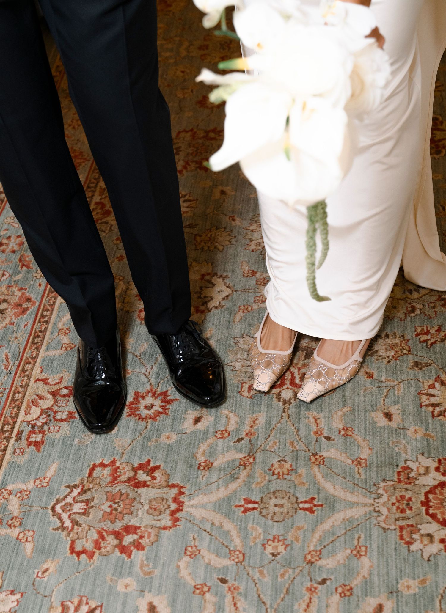Wedding party shoes lined up on a floral patterned carpet showing formal black dress shoes and white bridal footwear.
