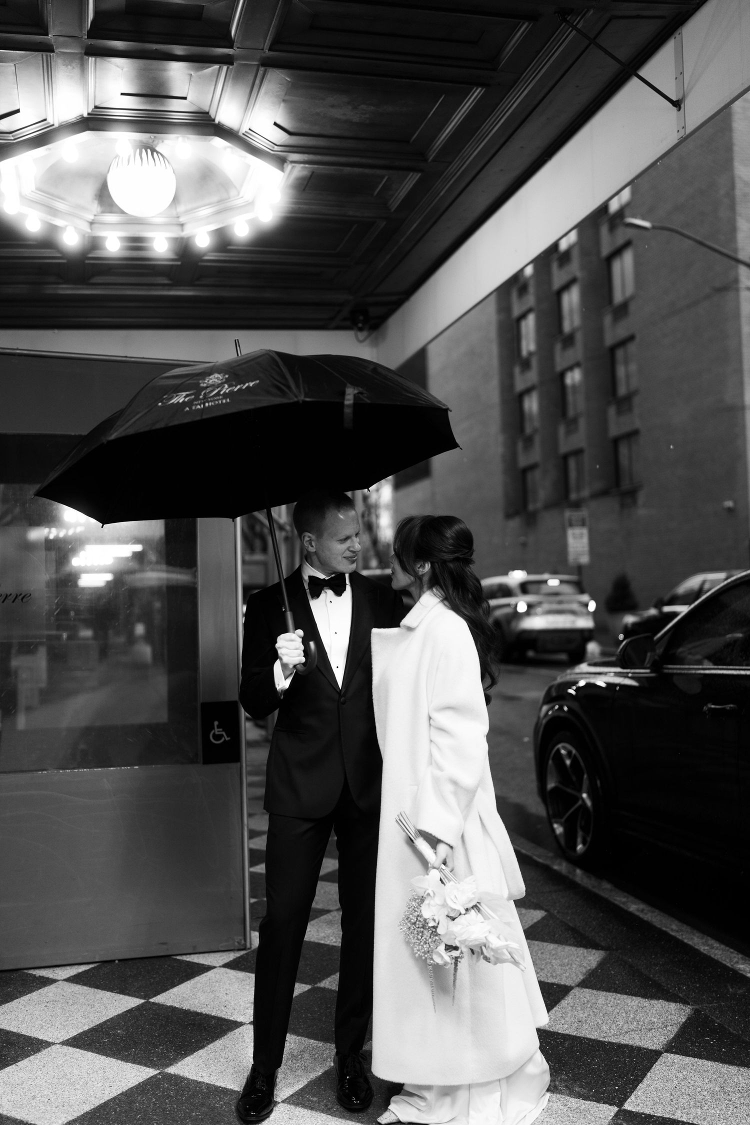 Black and white wedding photos showing couple walking under umbrellas on a checkered floor in an elegant venue.