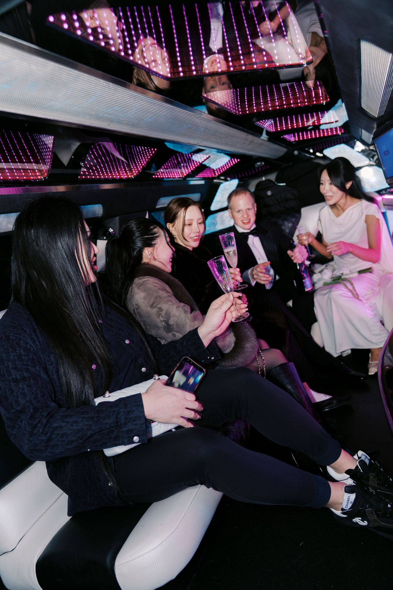 People sitting together in a dimly lit limousine interior with pink ambient lighting overhead.