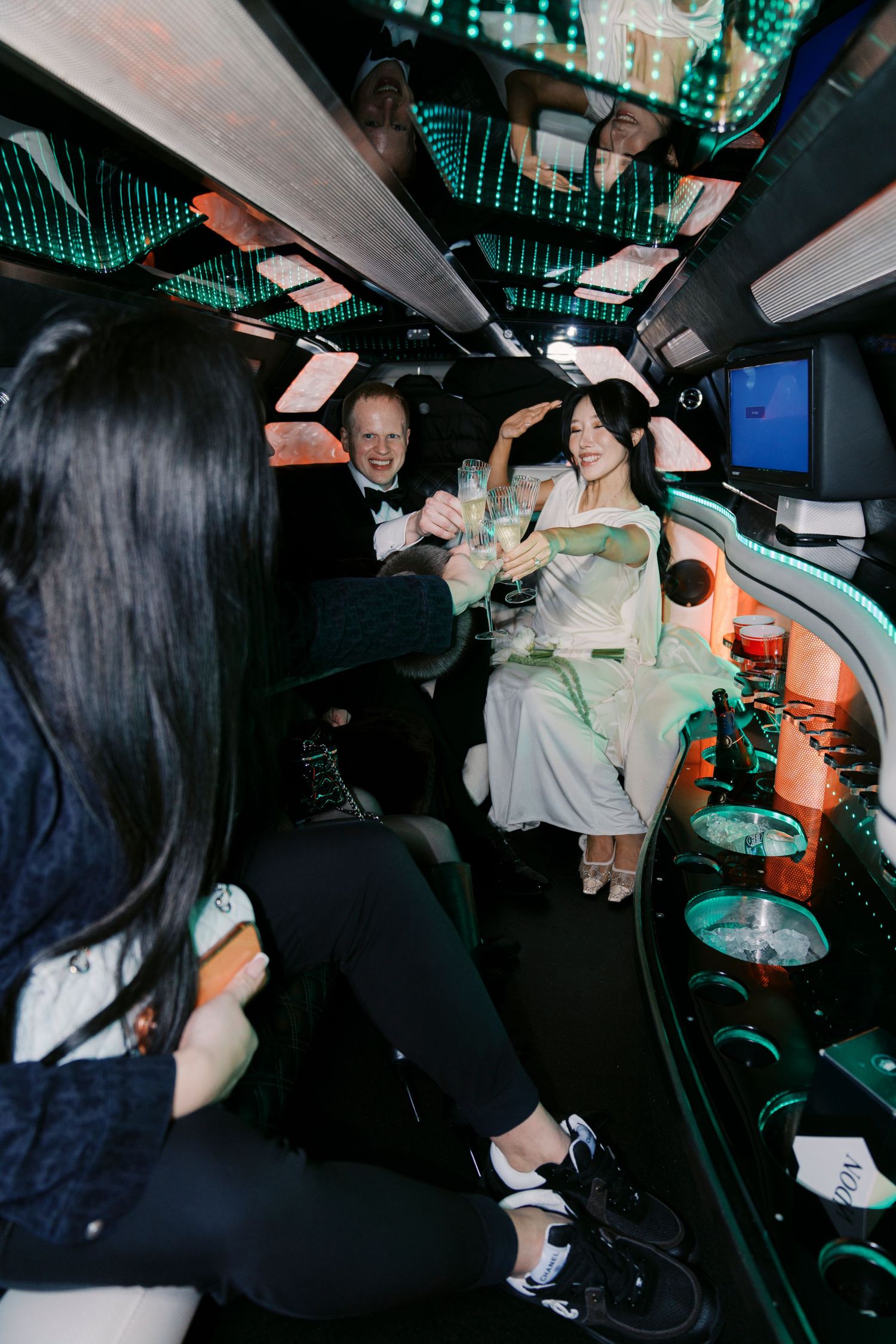 Party guests celebrate in a dimly lit limousine with neon green ambient lighting.
