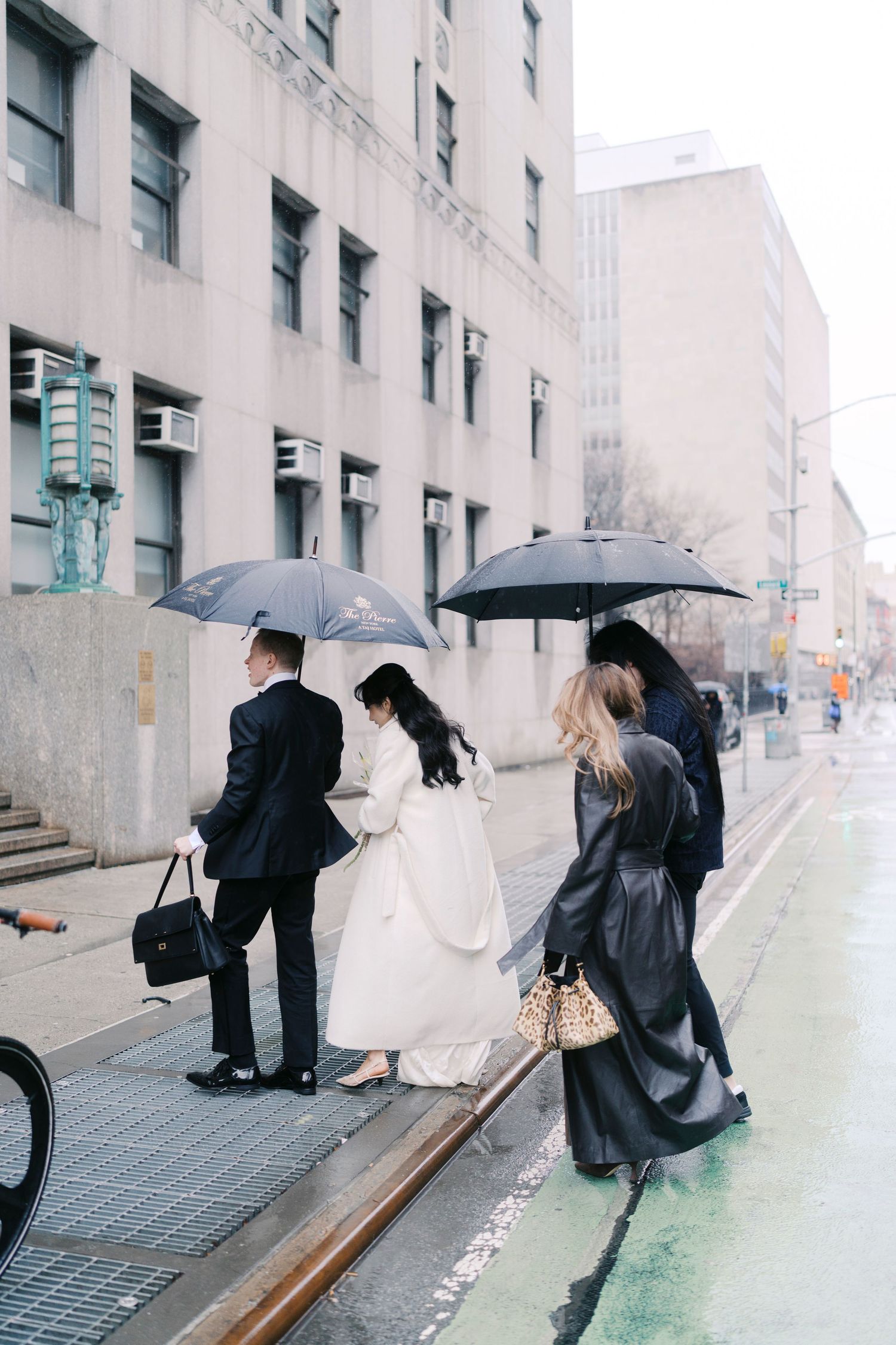 Wedding party walking along a city street with umbrellas on a rainy day.