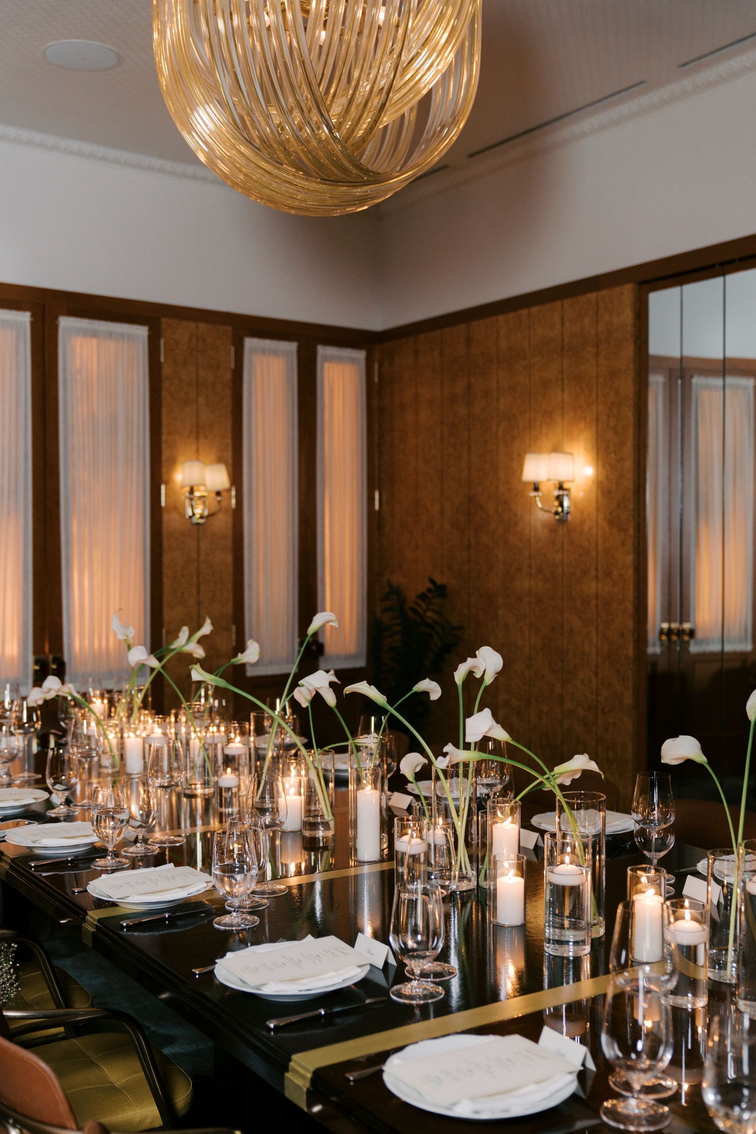 Formal dining table set with glowing candles, glass vases, and white place settings under golden pendant lights.