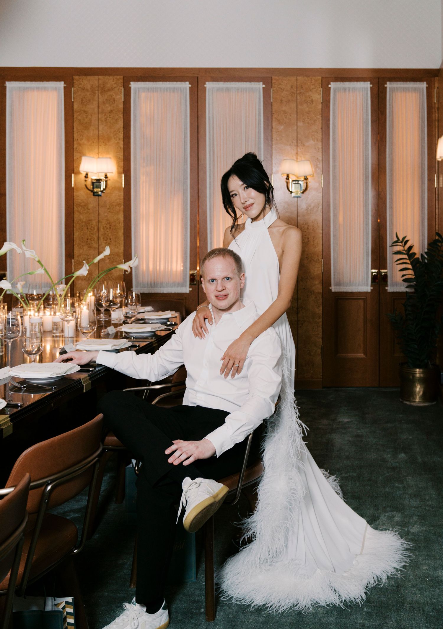 A couple in formal attire poses at an elegant reception venue with wood paneling and wall sconces.