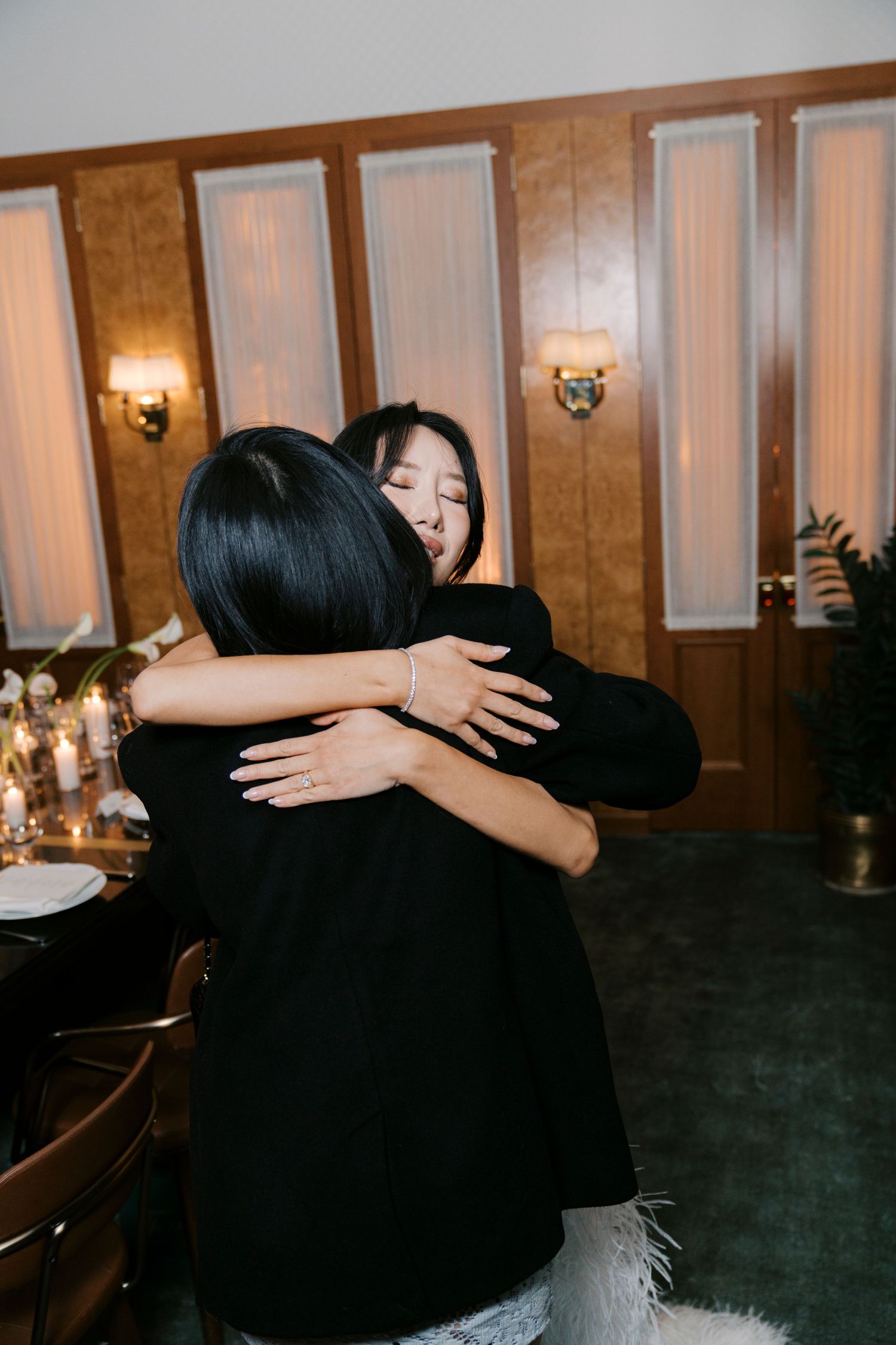 Two people share an emotional embrace at an elegant indoor venue with warm lighting.