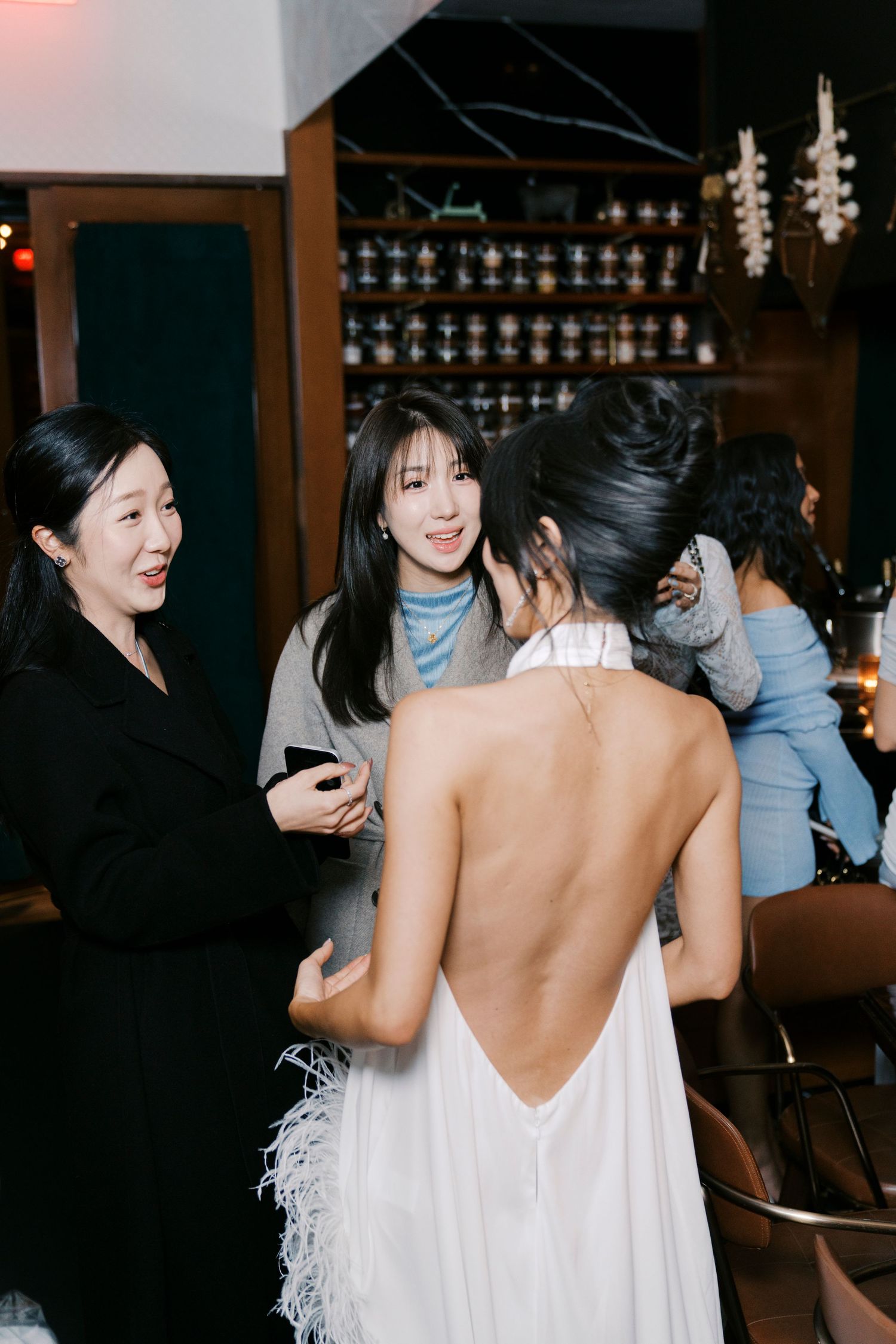 A group socializing at a bar with a woman in a backless white dress featuring feather details.