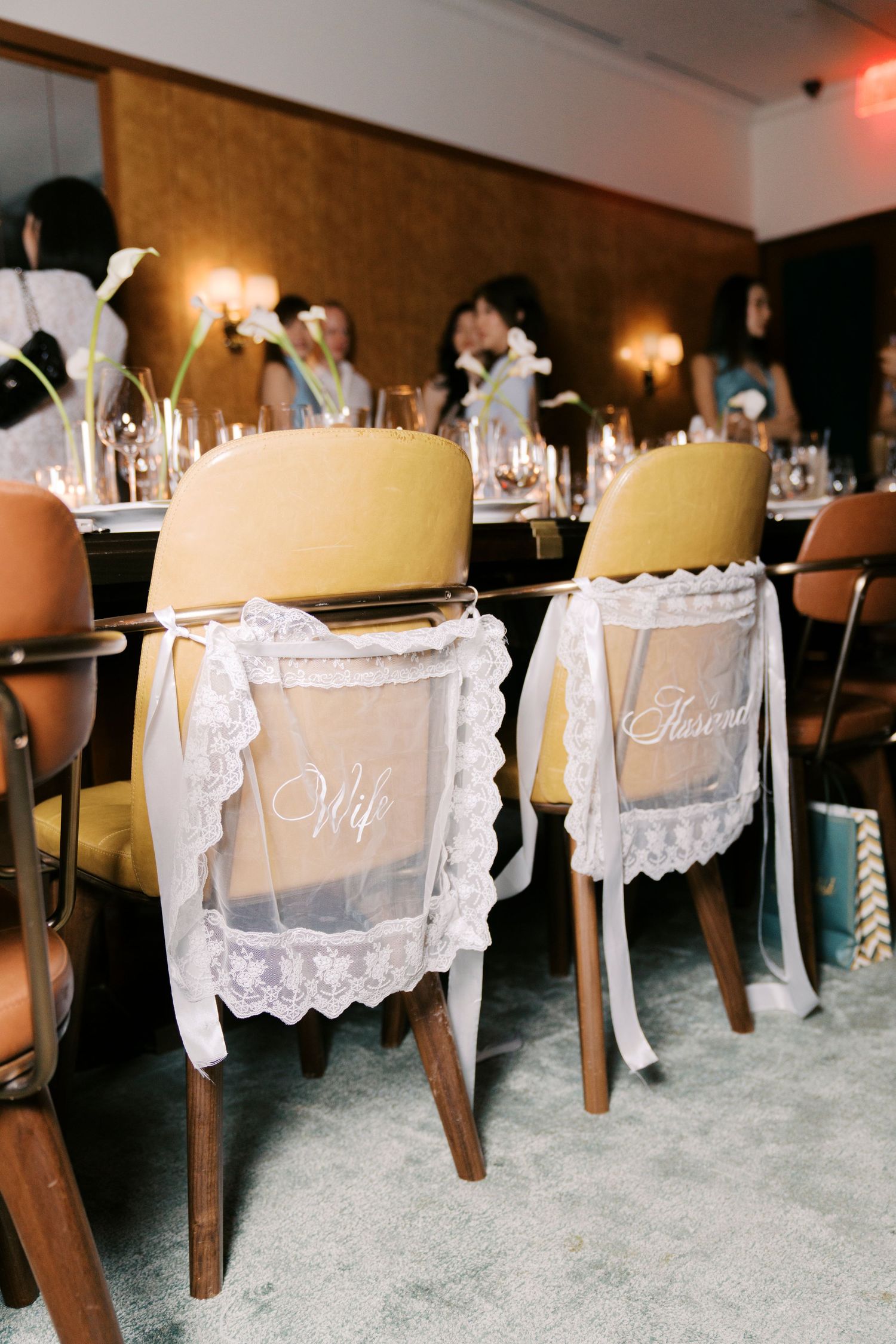 Vintage wooden chairs decorated with white lace signs for a wedding reception at an elegant indoor venue.