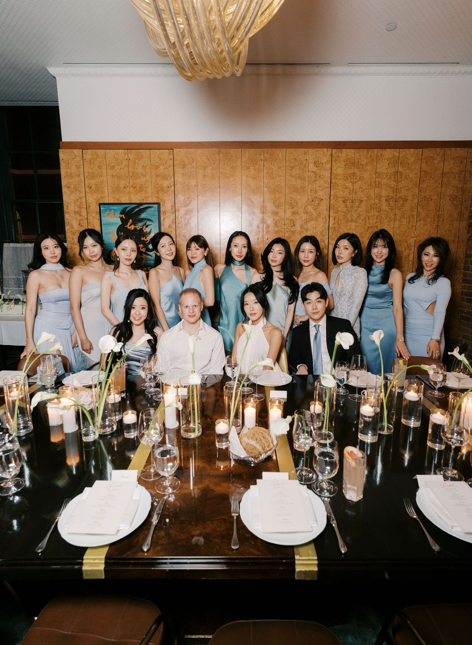 Wedding party gathered around an elegantly set dining table with crystal glassware and glowing candle centerpieces.