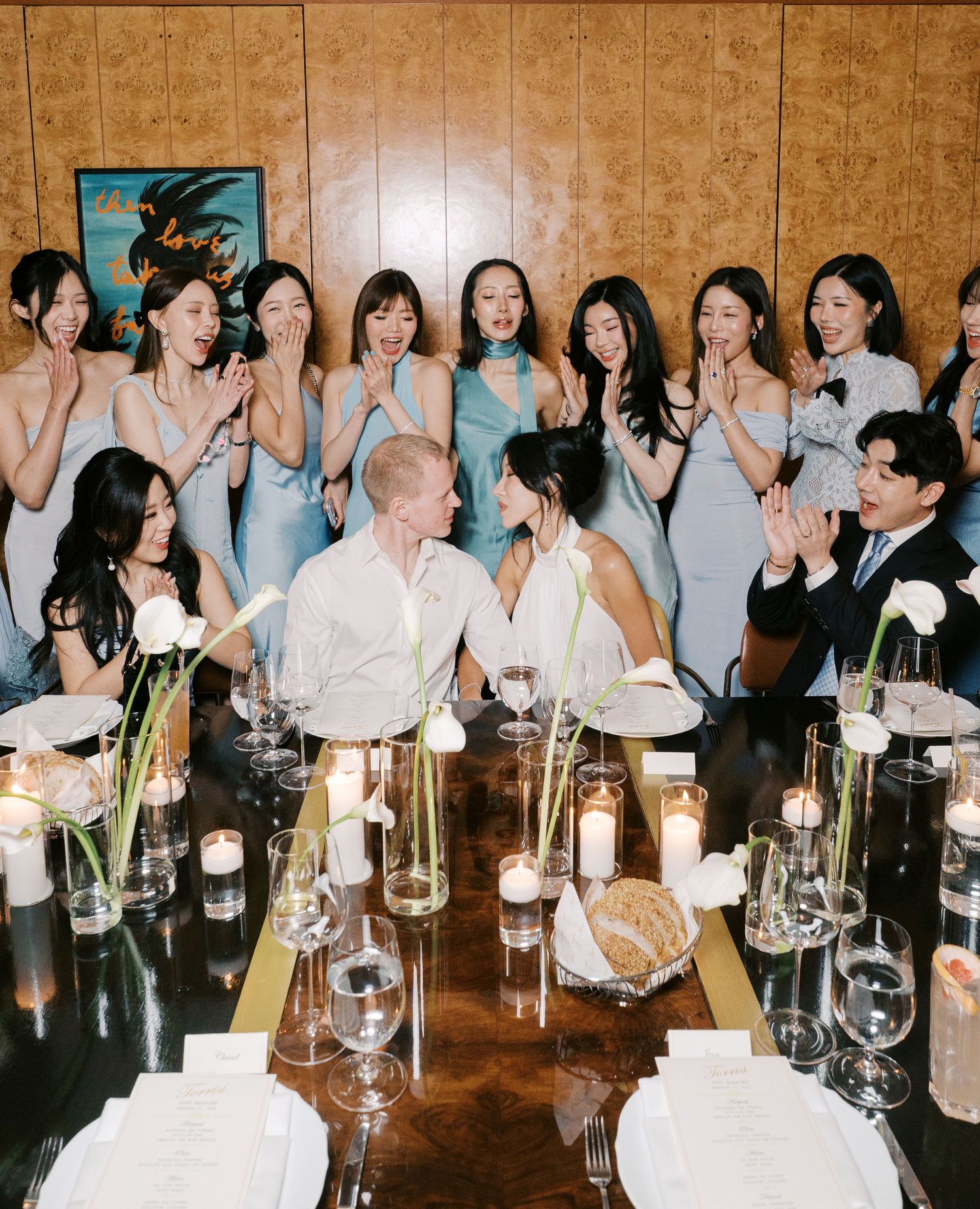 Wedding celebration at a restaurant table with bridesmaids in light blue dresses gathered around the newlyweds.