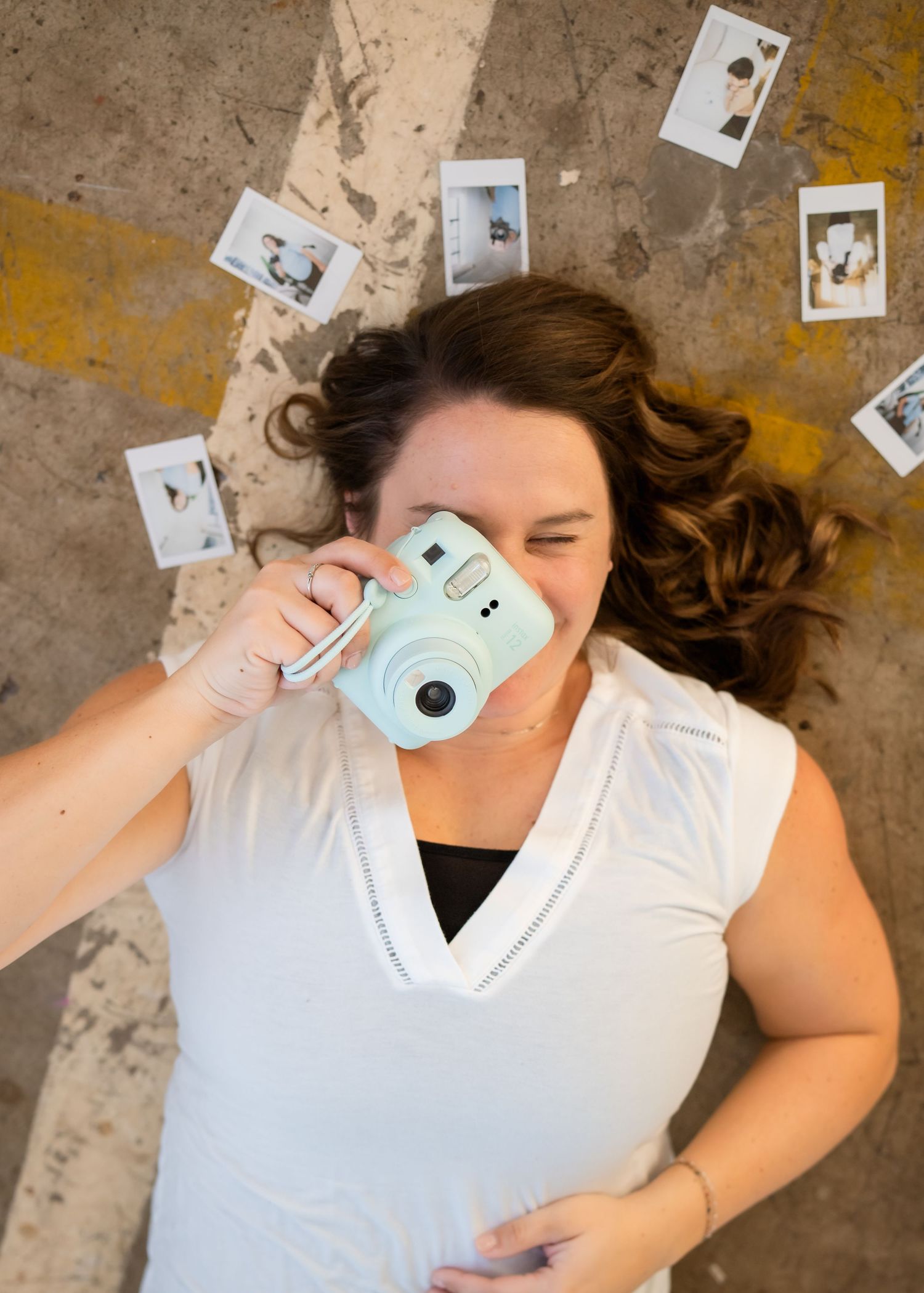 A series of photos showing someone lying on a concrete floor with a light blue Instax camera taking self portraits.