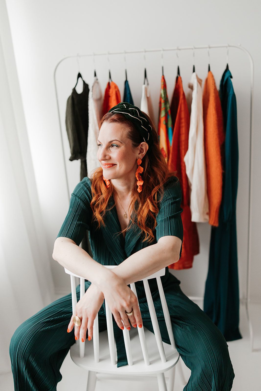 Casual portrait against white wall showing bright orange blazer, blue jeans, and gold hoop earrings.