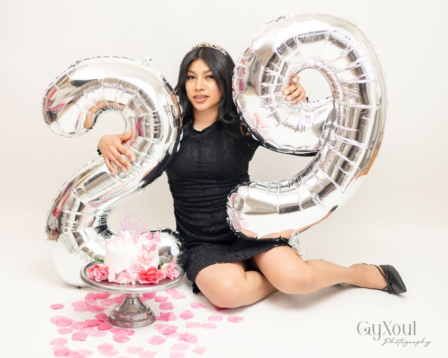 A celebratory scene with silver number balloons and pink rose petals scattered on a white floor.