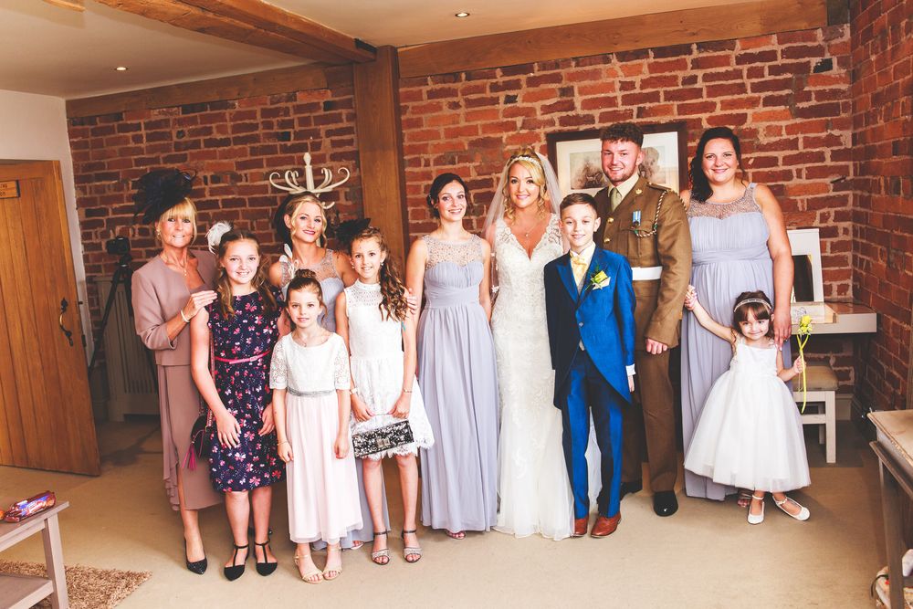 Wedding party lineup against exposed brick wall in formal attire.