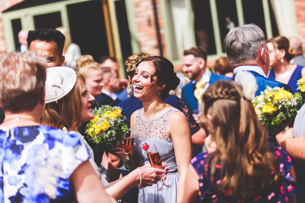 Outdoor wedding celebration with guests enjoying drinks and yellow bouquets in garden setting.
