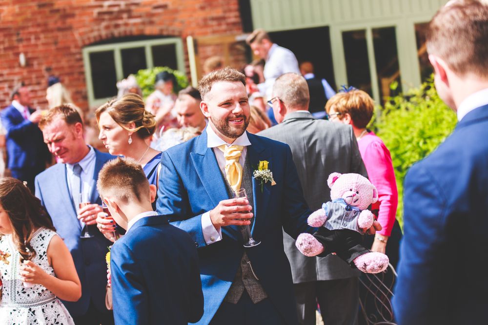 Wedding guests enjoying drinks and conversation during an outdoor reception by a brick building.
