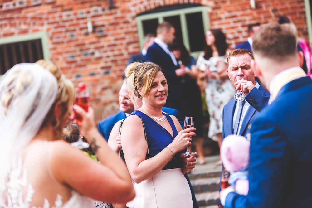 Wedding guests enjoying drinks and conversation during an outdoor reception by a brick building.