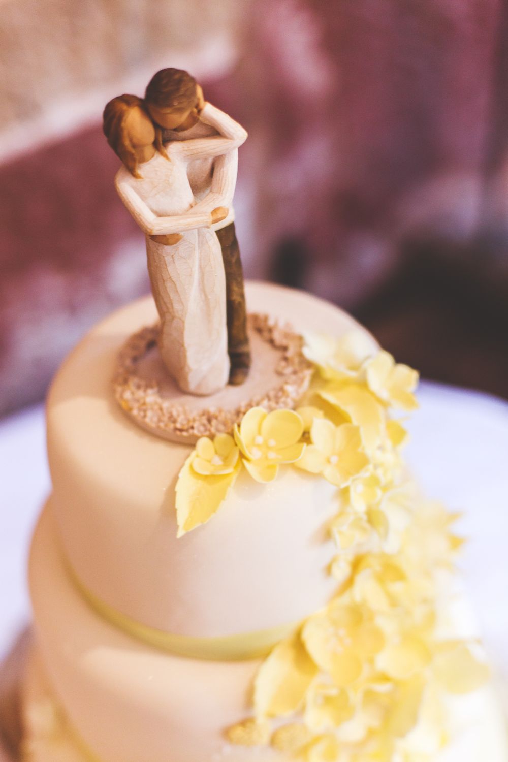 A white wedding cake topped with a Willow Tree figurine and decorated with cascading yellow flowers.
