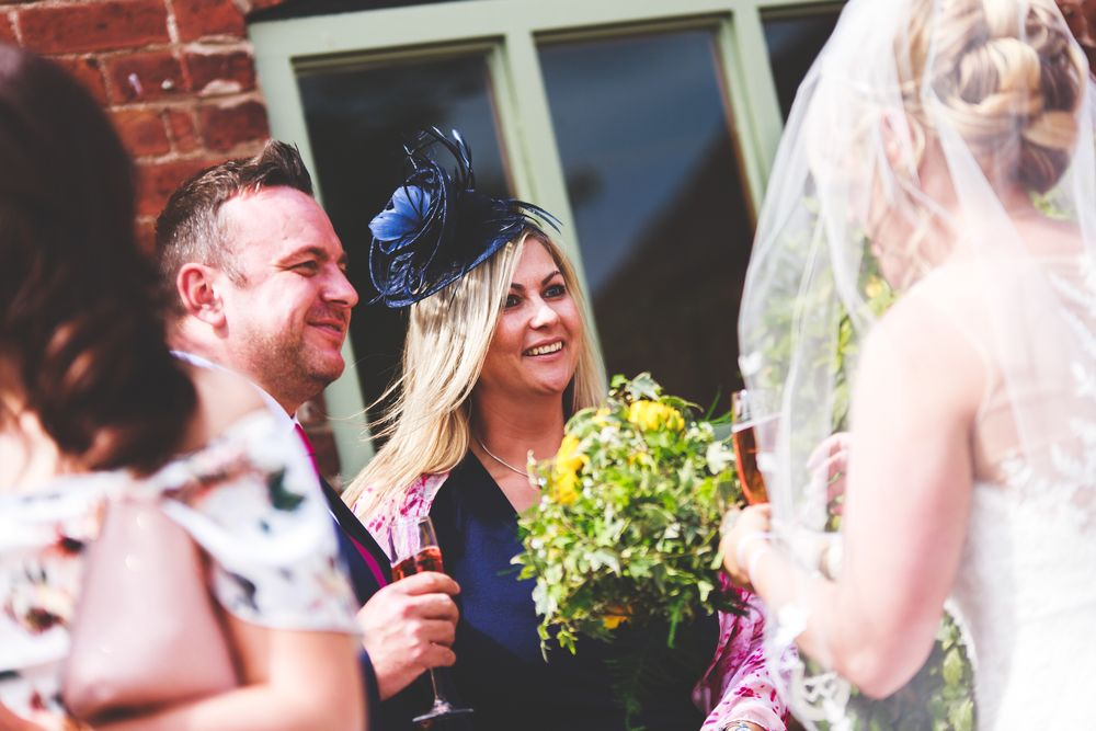 Wedding party guests laughing and celebrating outdoors with greenery in the background.