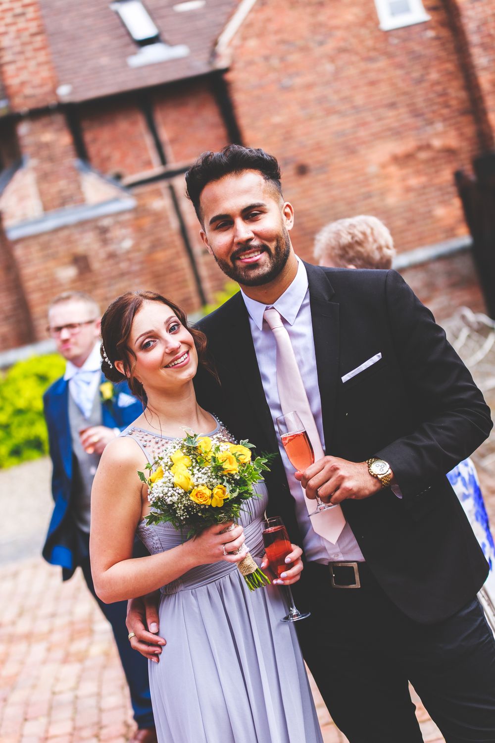 Wedding guests celebrate with yellow bouquet and formal attire at brick venue.